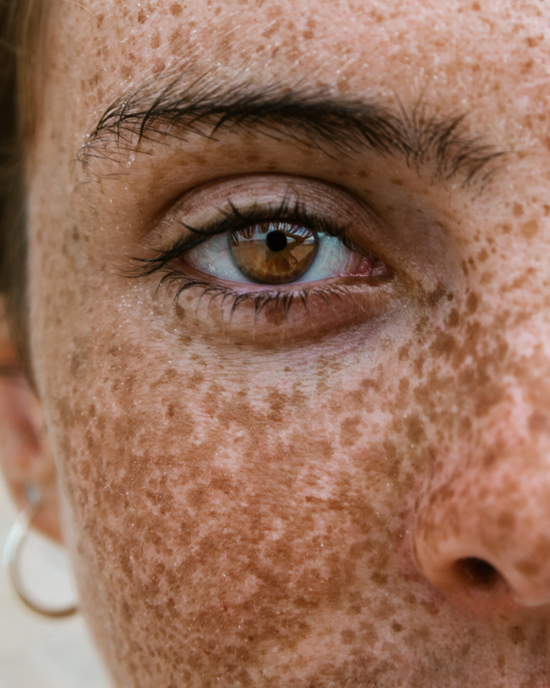 Nahaufnahme der Augenpartie eines weiblichen, natürlichen Gesichts mit Sommersprossen