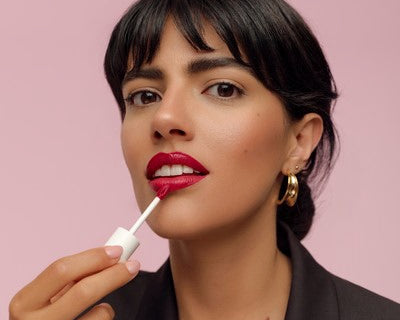 Frau trägt roten Liquid Lipstick auf vor rosa Hintergrund