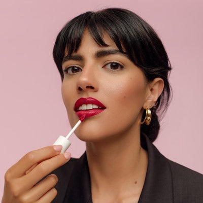 Frau trägt roten Liquid Lipstick auf vor rosa Hintergrund