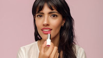 Frau trägt rosa Lippenstift auf vor rosa Hintergrund