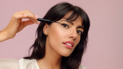 Frau trägt Eyeliner auf vor rosa Hintergrund