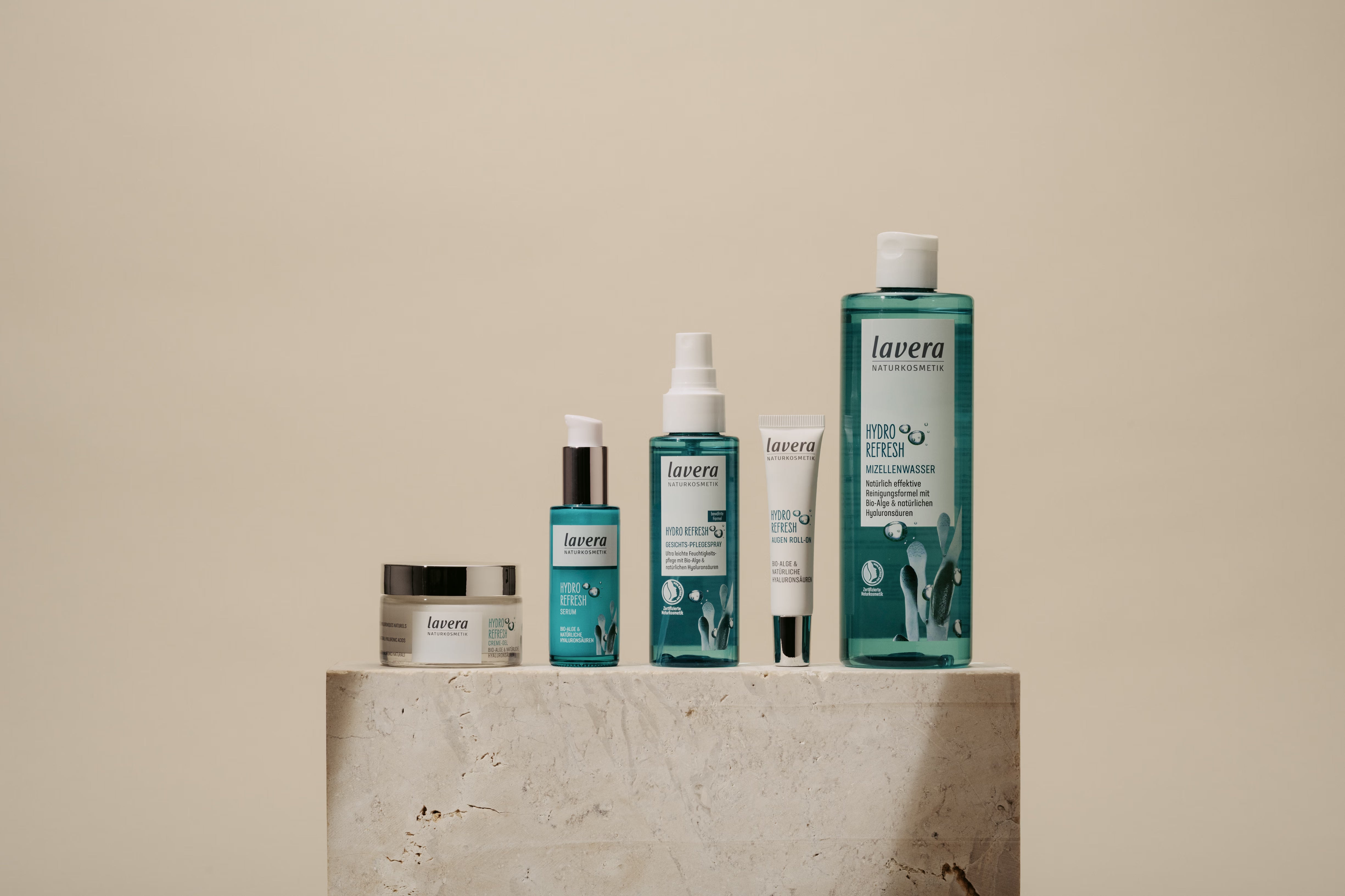 Six lavera Hydro-Refresh facial care products are displayed on a stone pedestal against a beige background.