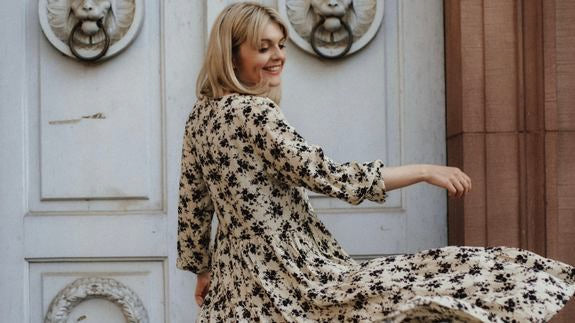 Frau dreht sich lachend im geblümten Kleid vor einer Tür