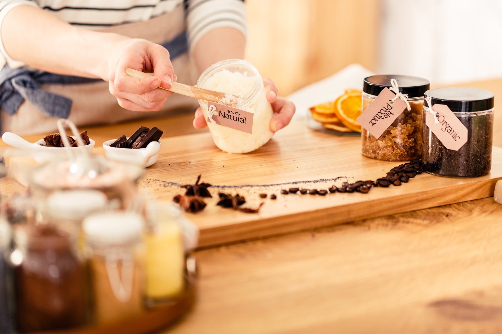 DIY Körperpeeling: Person füllt Zuckerpeeling ins Glas, Gewürze und Kaffee auf Brett
