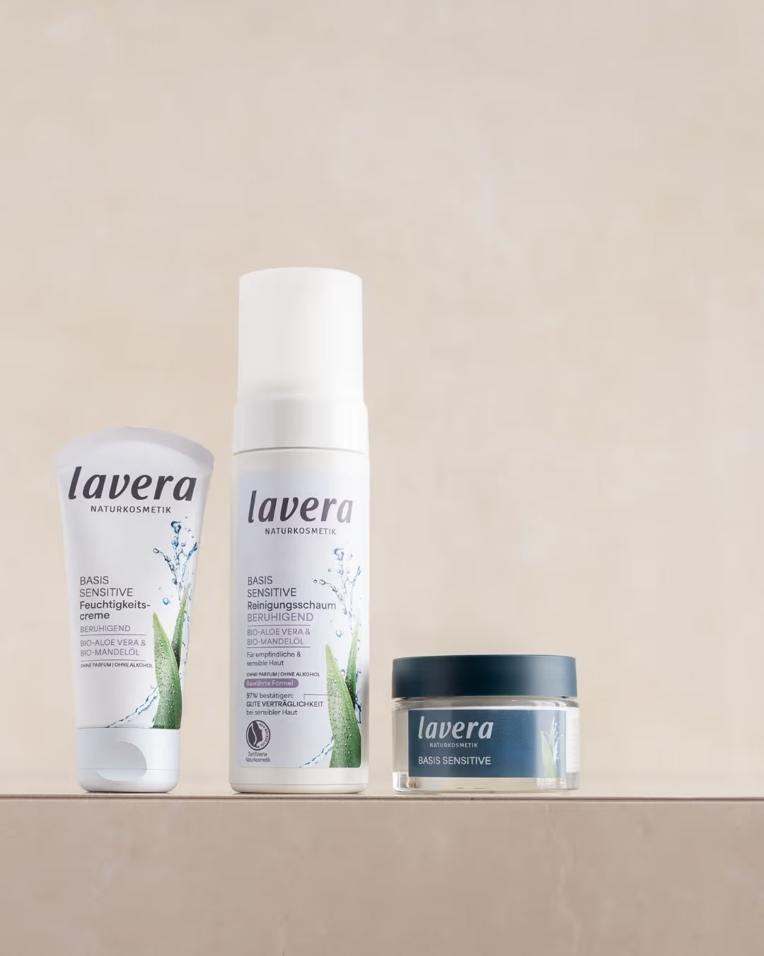 Three lavera basis sensitive skincare products - moisturizing cream, cleansing foam, and face cream - are placed side by side on a beige pedestal.
