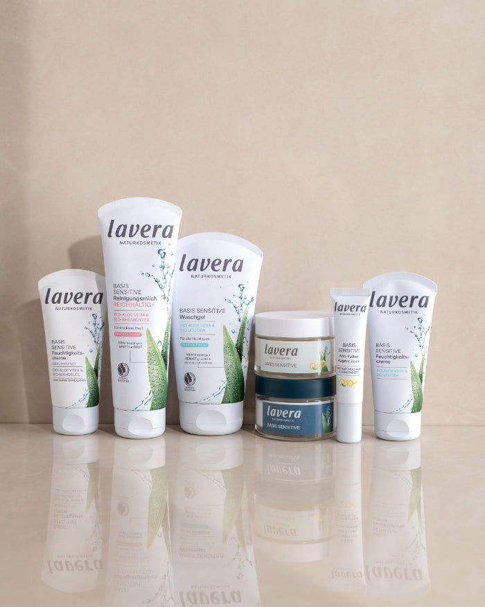 Several lavera BASIS SENSITIVE facial care products are arranged side by side on a reflective surface.
