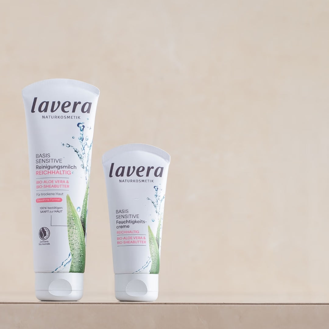 Two lavera basis sensitive skincare products - rich cleansing milk and moisturizing cream - are displayed on a beige pedestal.