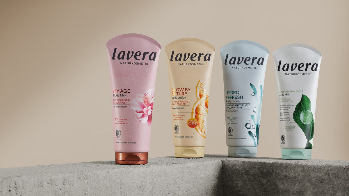 Four lavera body lotions from the My Age, Glow by Nature, Hydro Refresh and Barrier Balance ranges are displayed on gray concrete plinths against a neutral background.