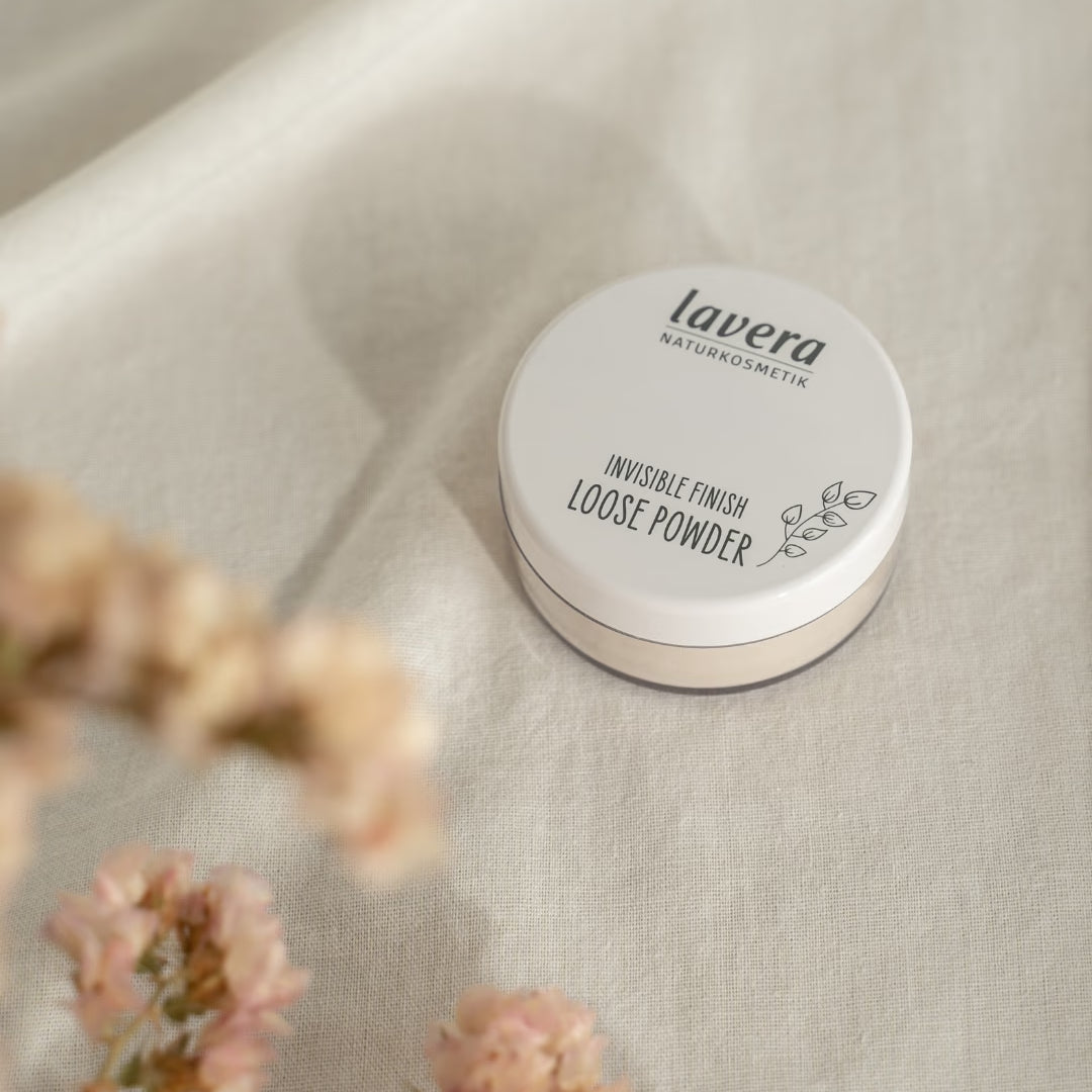 lavera Invisible Finish Loose Powder lies on light linen fabric, surrounded by blurred pink blossoms.