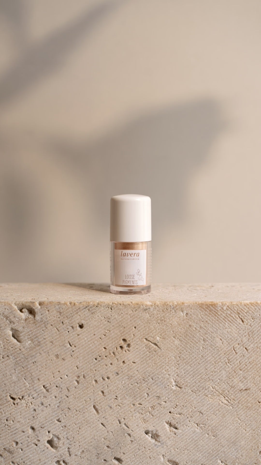 A bottle of lavera Liquid Eyeliner stands on a light-colored stone block in front of a softly lit beige background.
