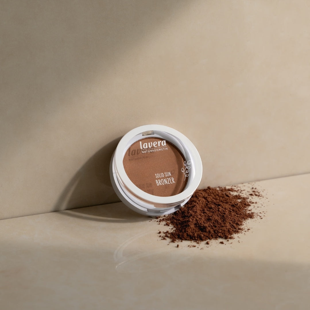 lavera Solid Sun Bronzer lies on a beige-colored surface beside scattered bronzing powder.