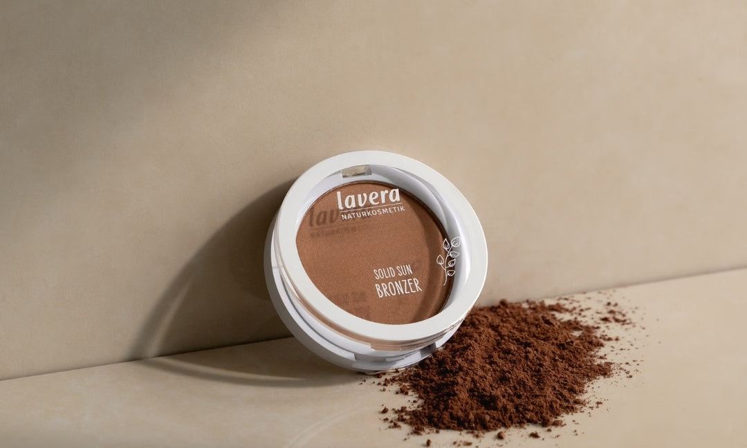lavera Solid Sun Bronzer lies on a beige-colored surface beside scattered bronzing powder.