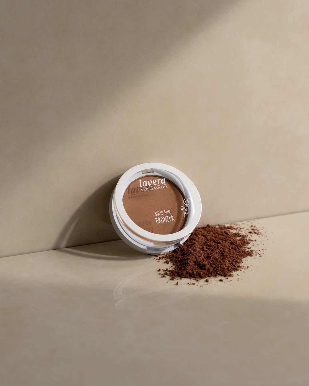 lavera Solid Sun Bronzer lies on a beige-colored surface beside scattered bronzing powder.