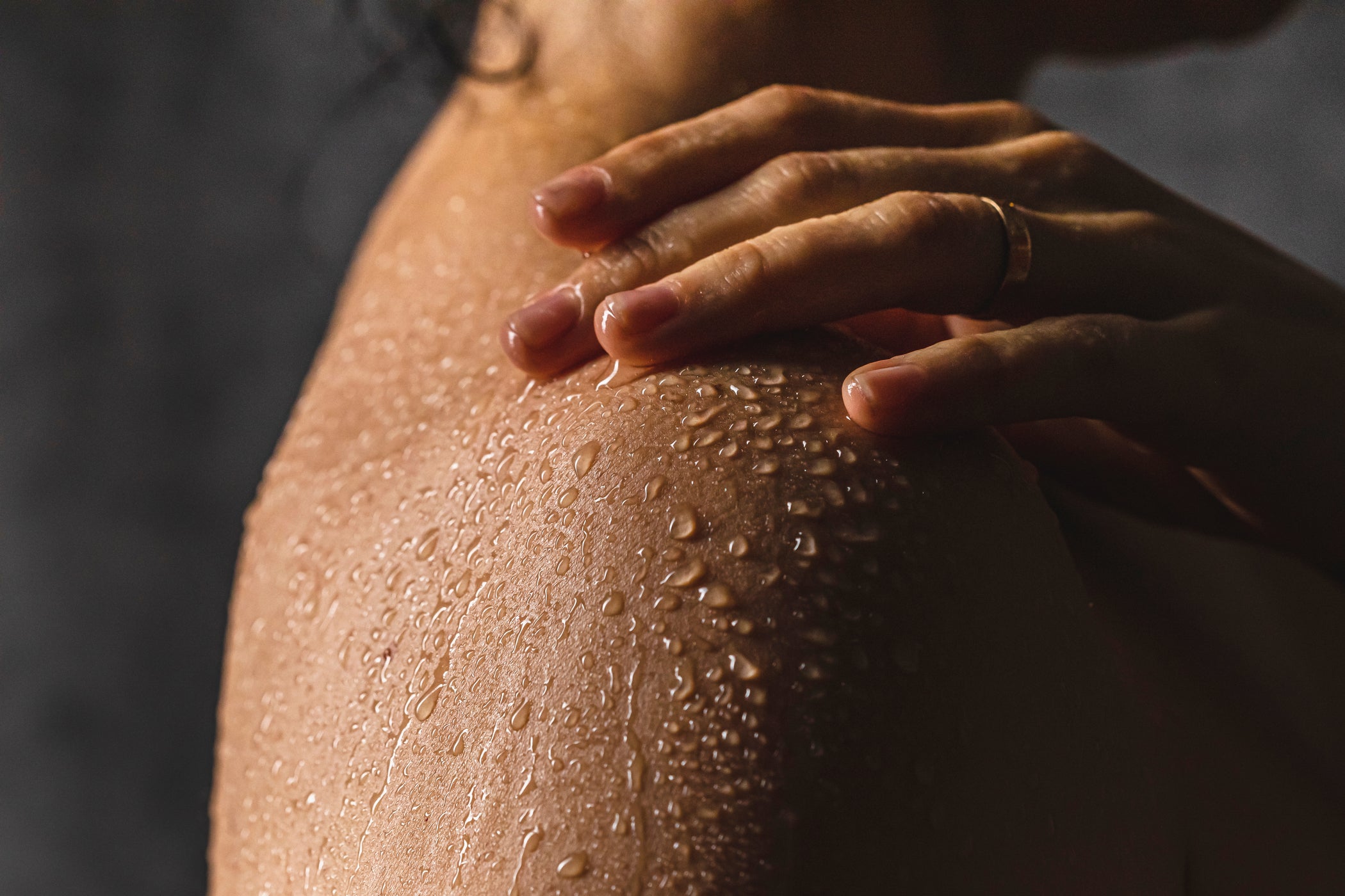 Nahaufnahme der Schulterpartie einer weiblichen Person, die mit Wassertropfen übersät ist – bei dunklem Hintergrund