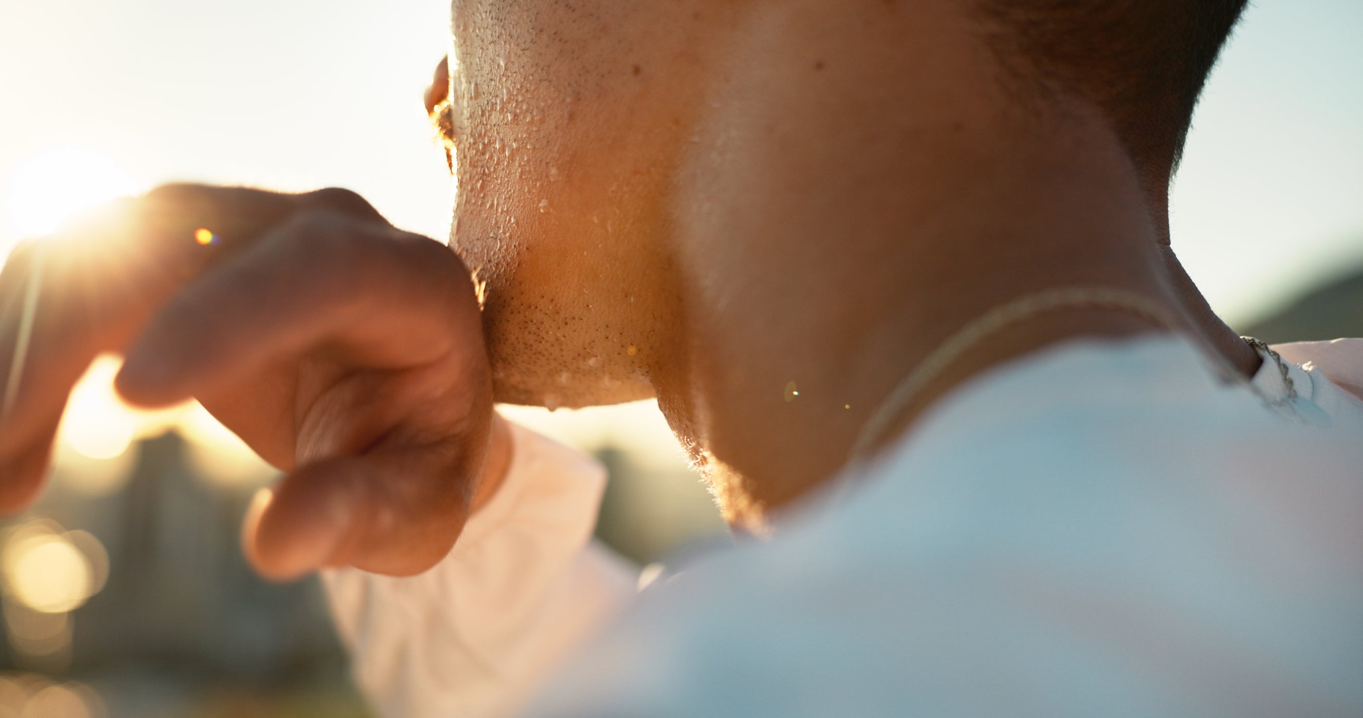 Mann wischt Schweiß mit Handtuch vom Gesicht, Sonnenlicht im Hintergrund