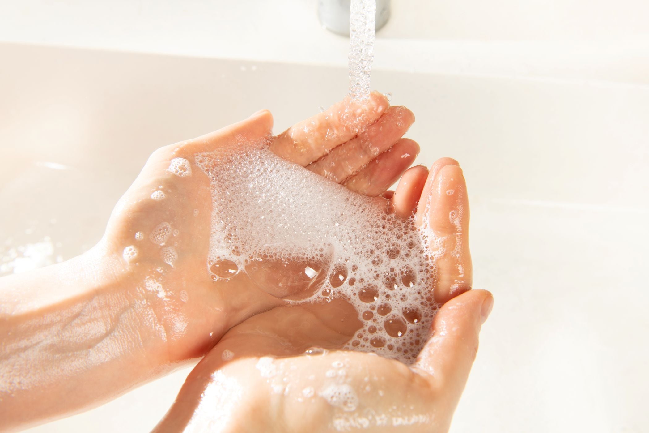Hände unter einem laufenden Wasserhahn, die mit Seifenschaum bedeckt sind