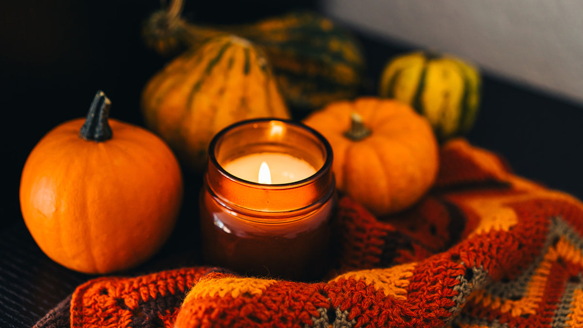 Brown candle jar with pumpkins and a crocheted blanket in warm colors