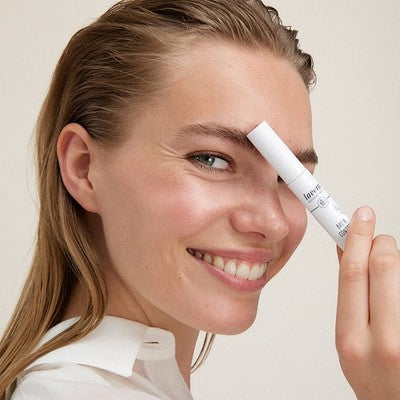 Lächelnde Frau hält lavera Make-up-Stift an die Augenbraue, Nahaufnahme