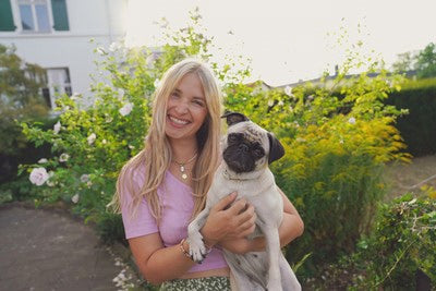 Blonde Frau lächelt und hält Mops im Arm