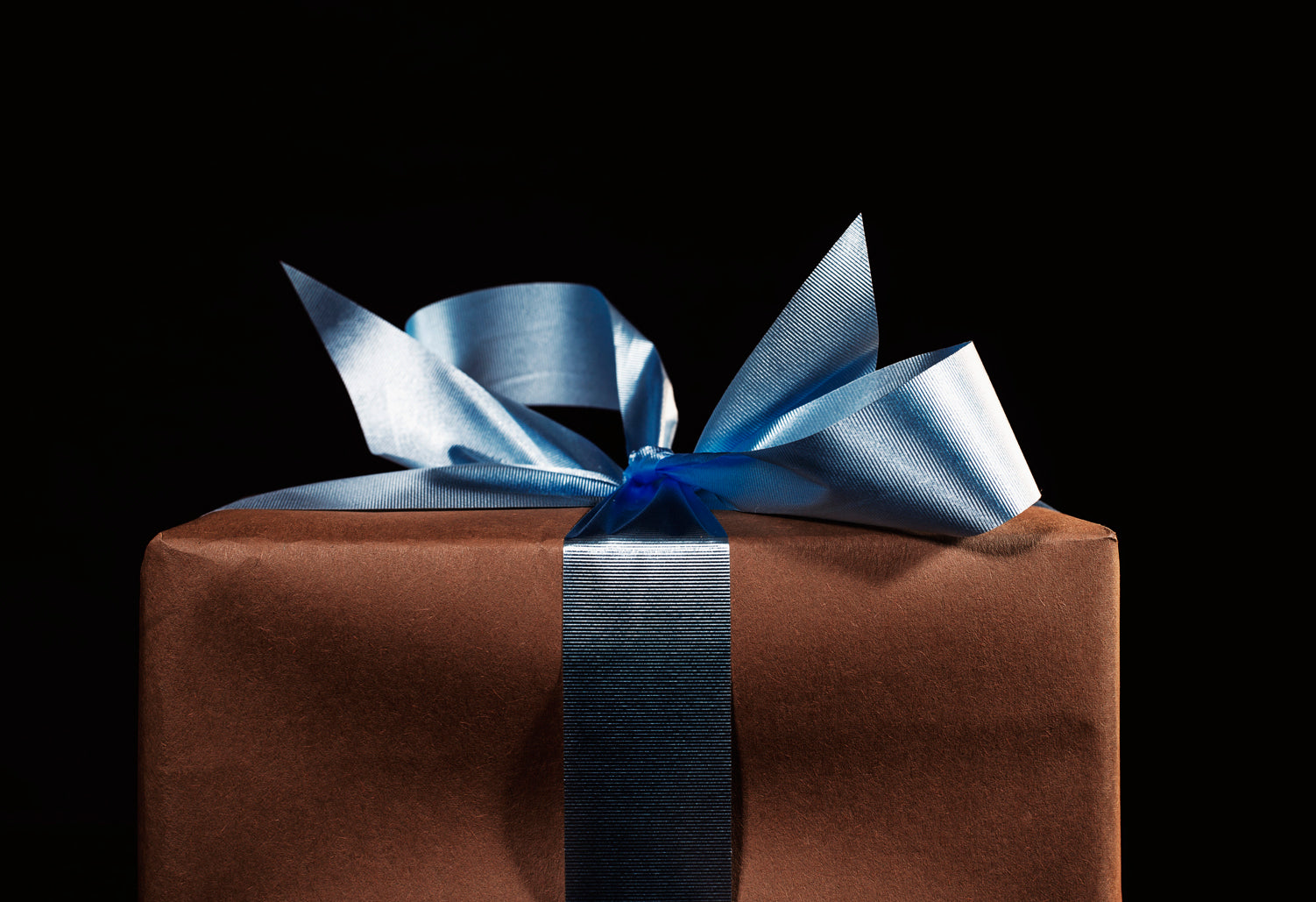 Geschenk in braunem Papier mit blauer Schleife vor schwarzem Hintergrund