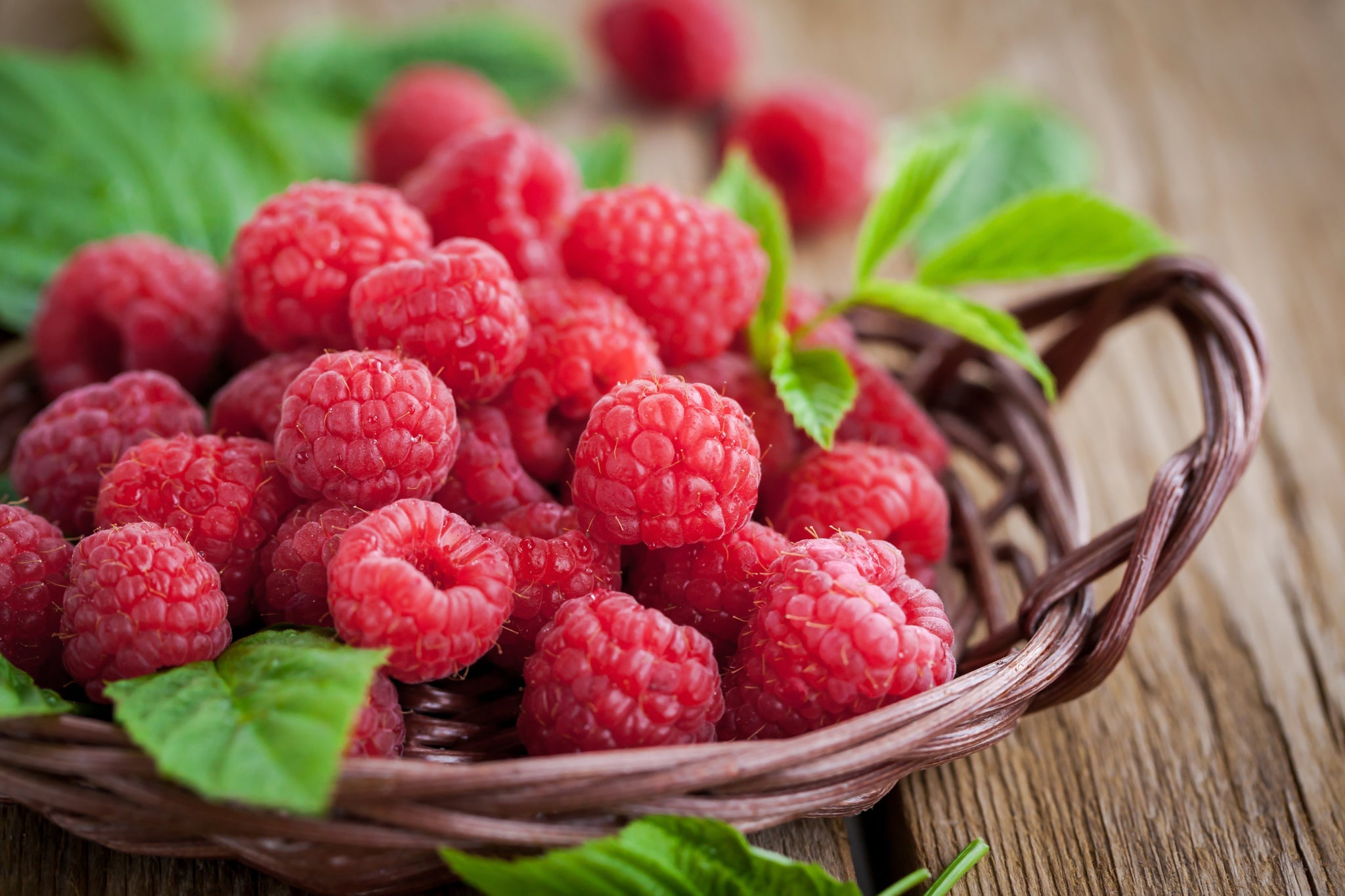 Korb voller Himbeeren mit grünen Blättern auf Holzuntergrund