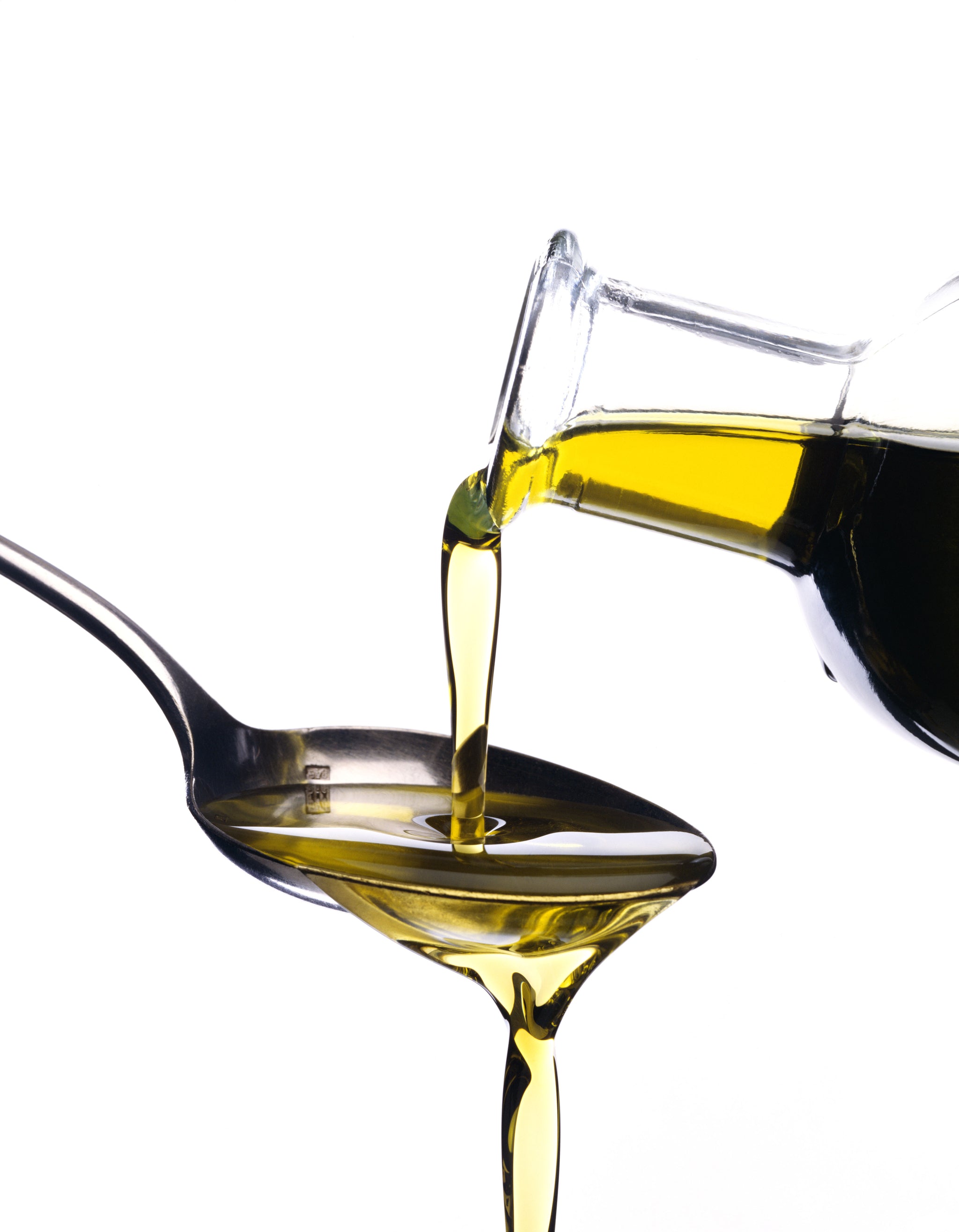 Olivenöl, das aus einer Flasche in einen Löffel gegossen wird