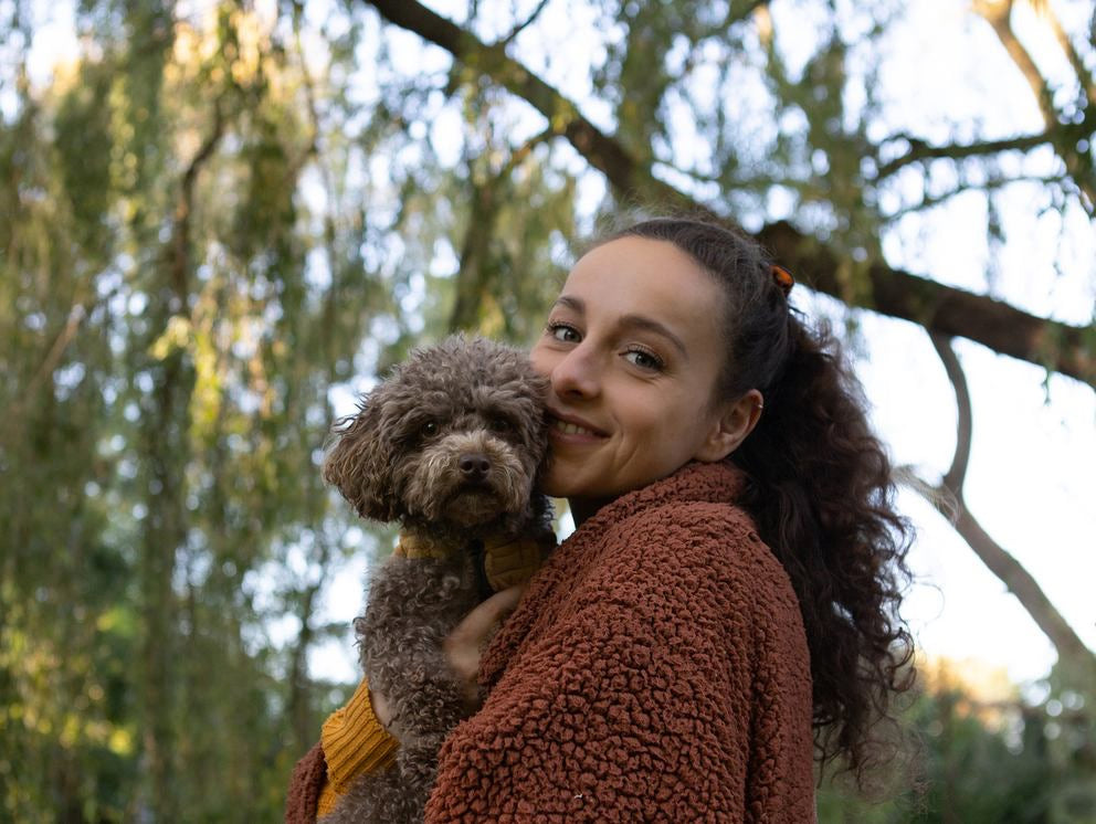 Frau umarmt kleinen Hund im Grünen und lächelt