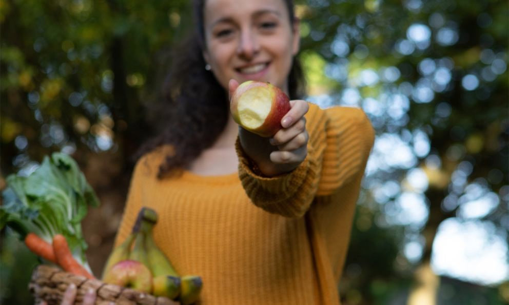 Frau hält angebissenen Apfel und Korb mit Obst und Gemüse