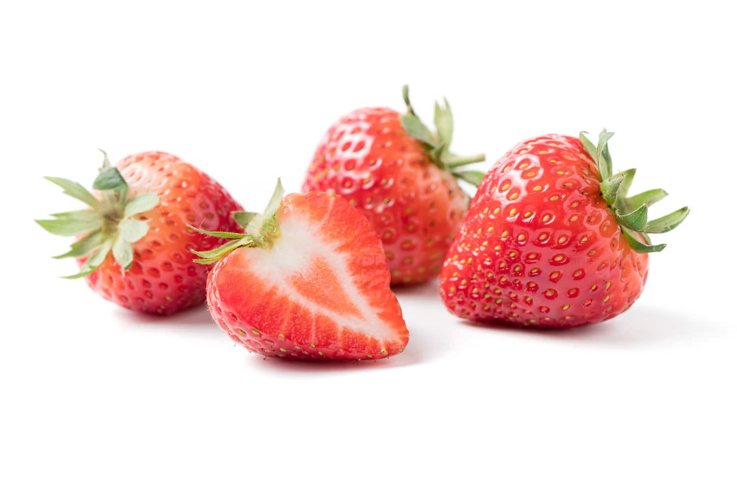 Erdbeeren enthalten wichtige Mineralstoffe und Vitamine Drei ganze und eine aufgeschnittene Erdbeere mit grünen Blättern auf weißem Hintergrund