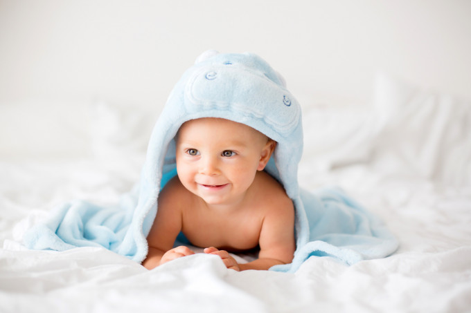 Baby und Kinder Wundschutz Kategoriebild Baby in Handtuch liegt auf dem Bett , guckt in die Kamera und lacht
