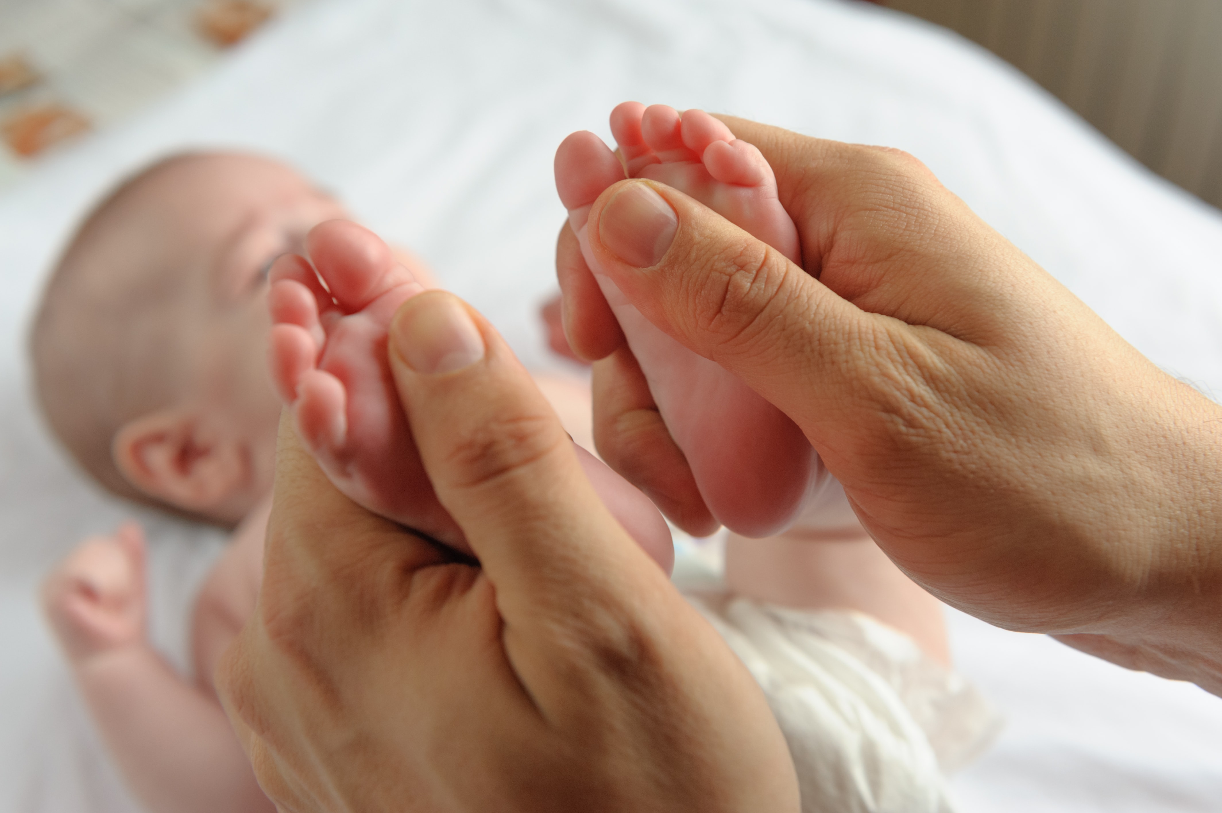 Ein Baby liegt auf dem Rücken auf einer Decke und wird an beiden Füßen massiert.