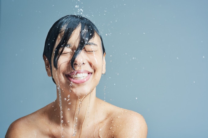 Gesichtsreinigung Kategoriebild Frau lacht während Wasser auf den nassen Kopf herab faellt