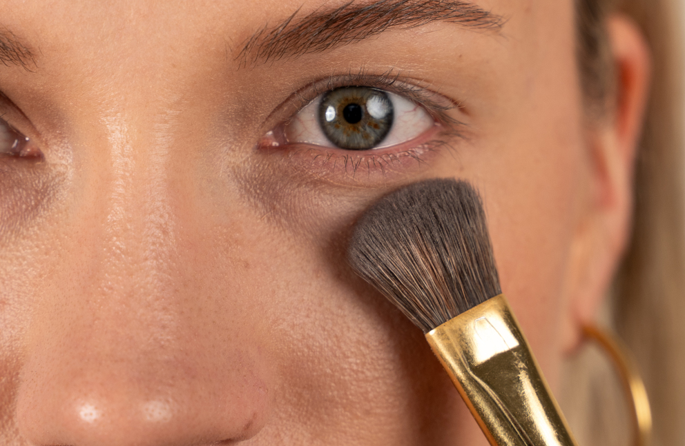 Frontal view of a woman's face with a makeup brush under her eye