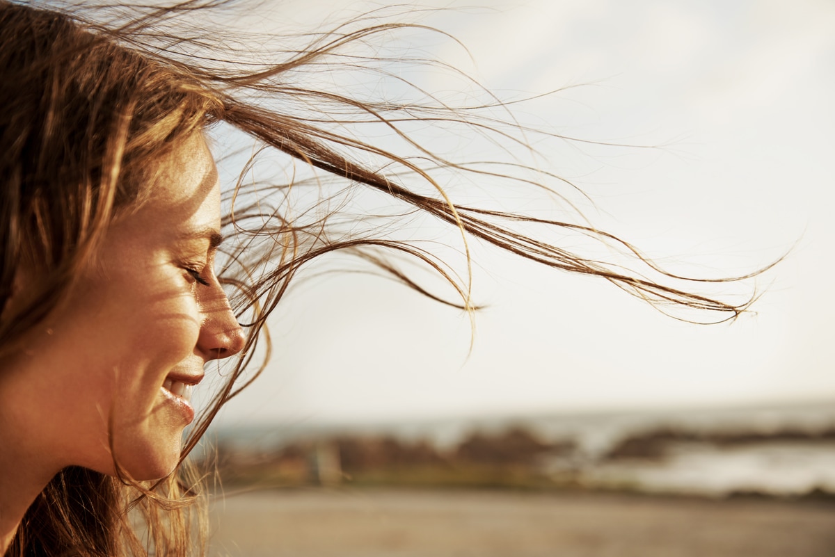 So pflegst du dein feines Haar Aufnahme einer jungen Frau im Profil, ihr Haar wird vom Wind durch die Luft geweht