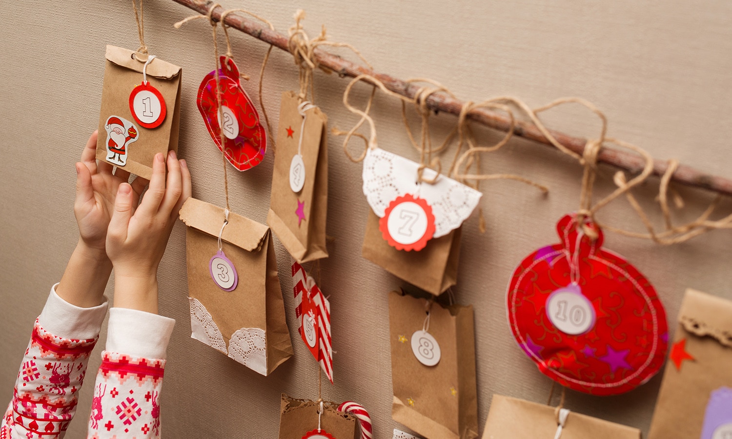 An der Wandhängender selbstgebastelter Adventskalender aus kleinen unterschiedlich großen Papiertüten, ein Kind hält eines in den Händen