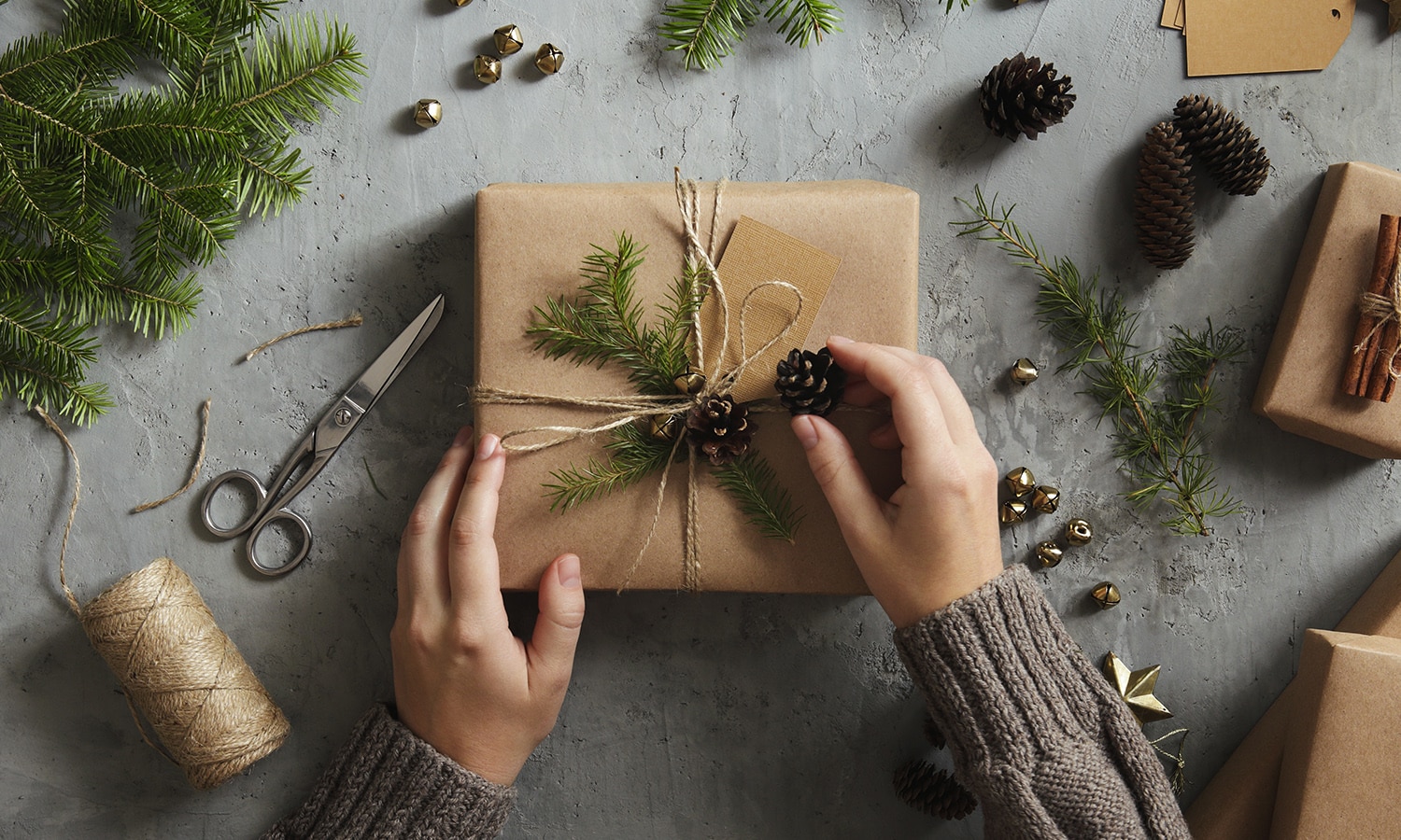 Frauenhände verzieren ein Weihnachtsgeschenk mit einer Kordel und Tannenzweigen